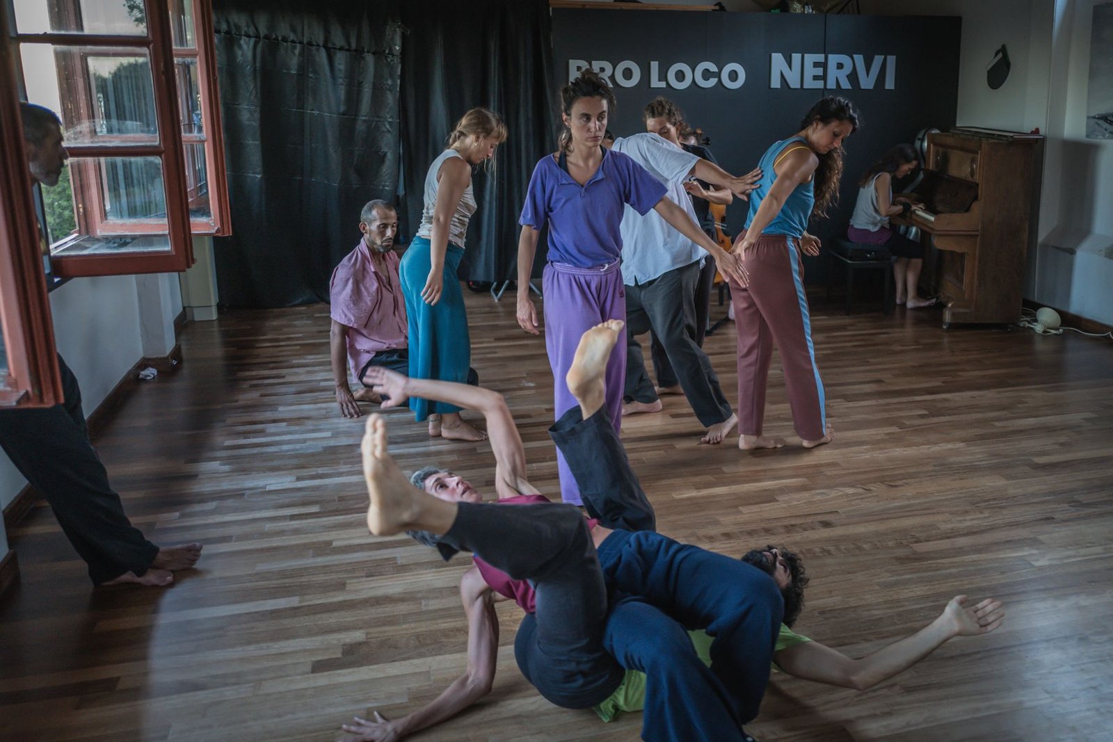 Dancers sharing weight on a wooden studio floor while a pianist plays